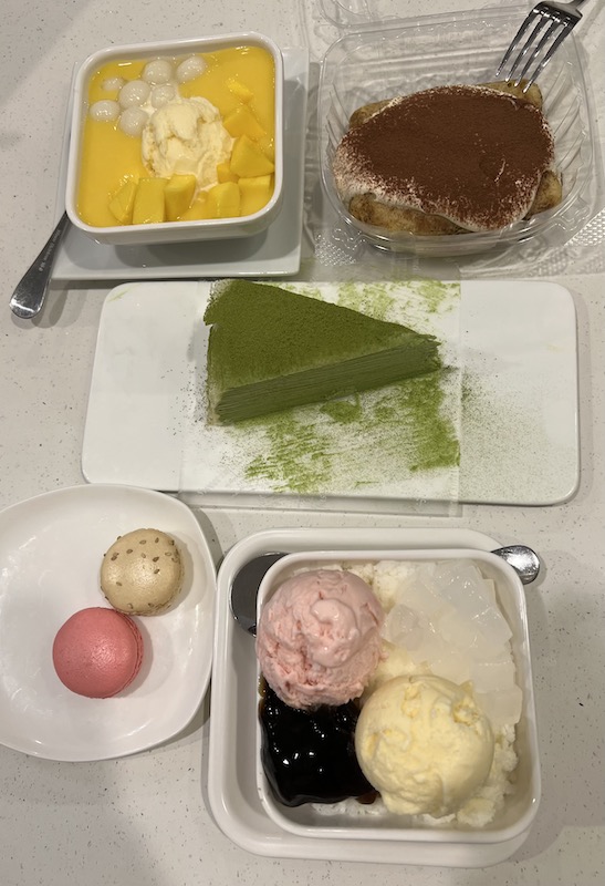 A table of various desserts: sago, tiramisu, crepe cake, macarons, etc.