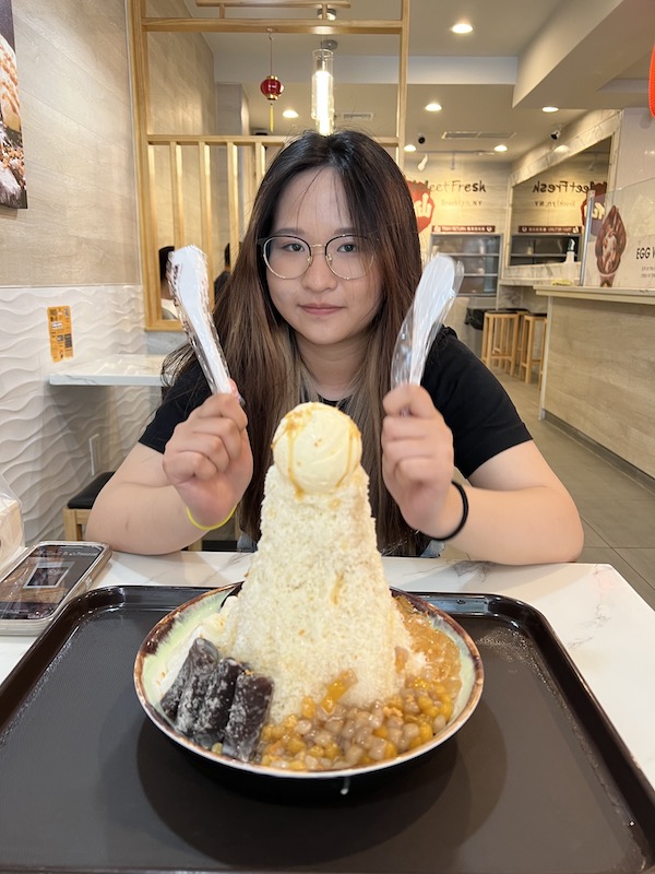 A large bowl of shave ice, a girl holding utensils behind.