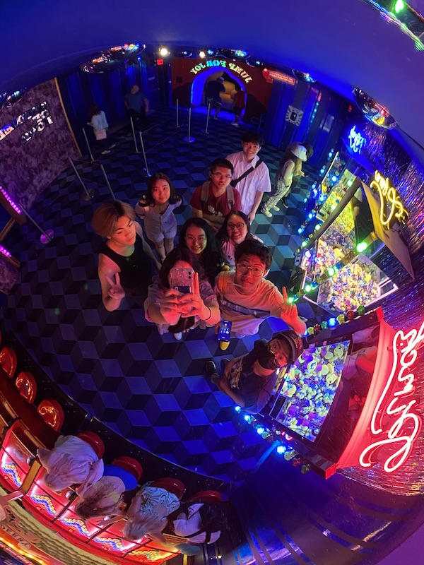 A mirror selfie on a drop-in dome in an arcade like setting
                      	with a group of college kids