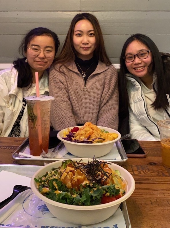 Three girls positing for a pictures with poke bowls in front of them.