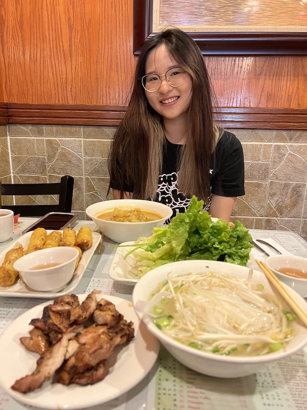 Girl posing with vietminese food on the table: curry chicken with rice, spring rolls, and pho.